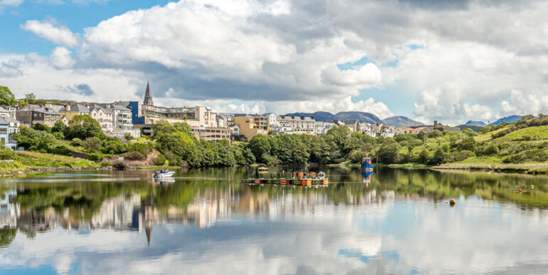 Clifden harbor at high tide with clouds reflecting in the water and the village in the background