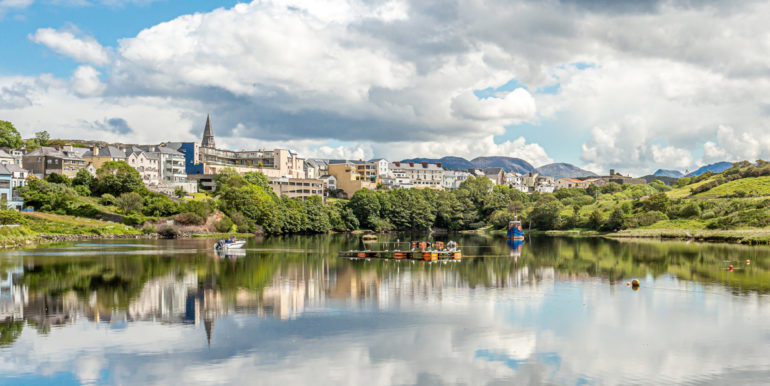 Clifden harbor at high tide with clouds reflecting in the water and the village in the background